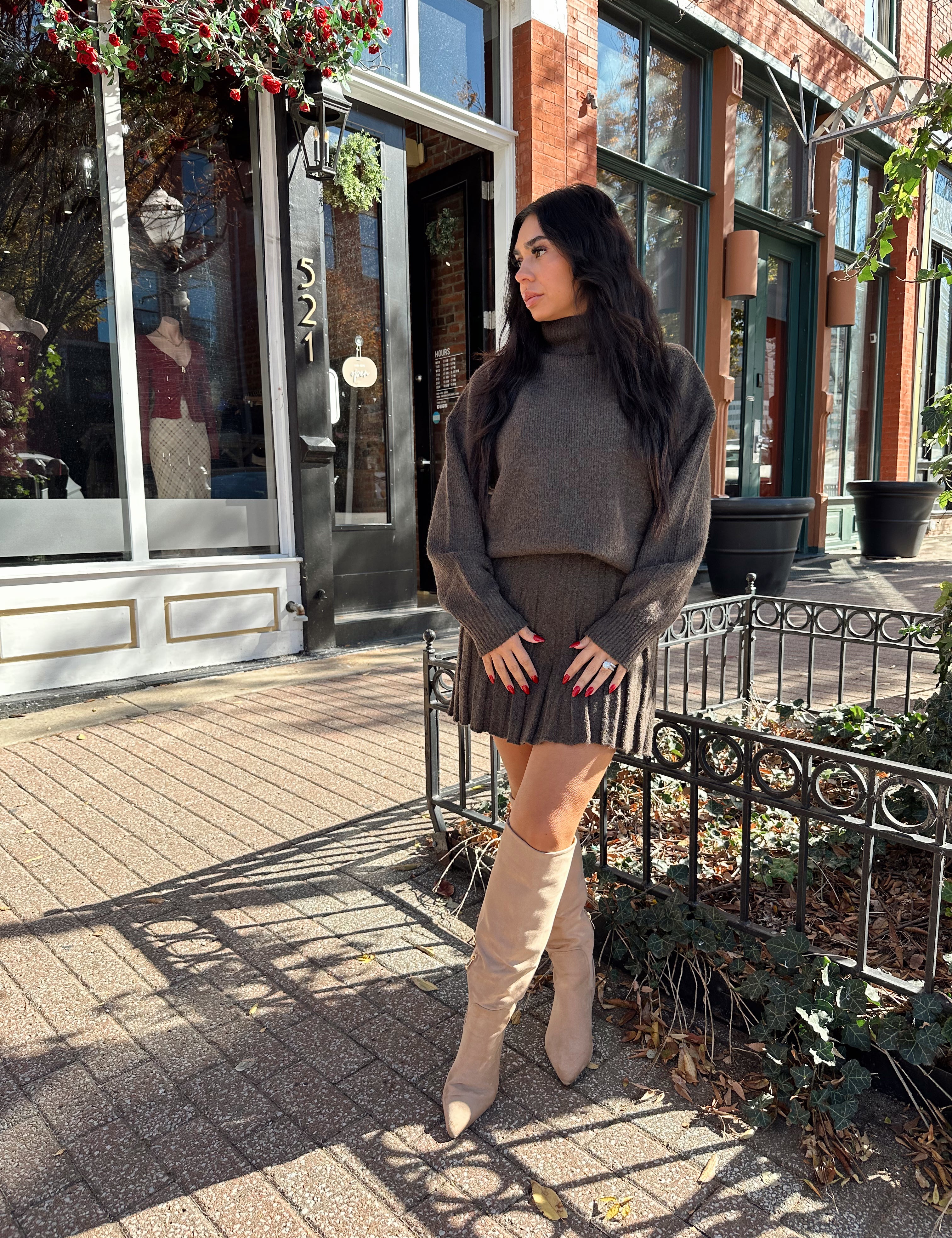 Woman wearing brown sweater two piece set with pleated mini skirt. 