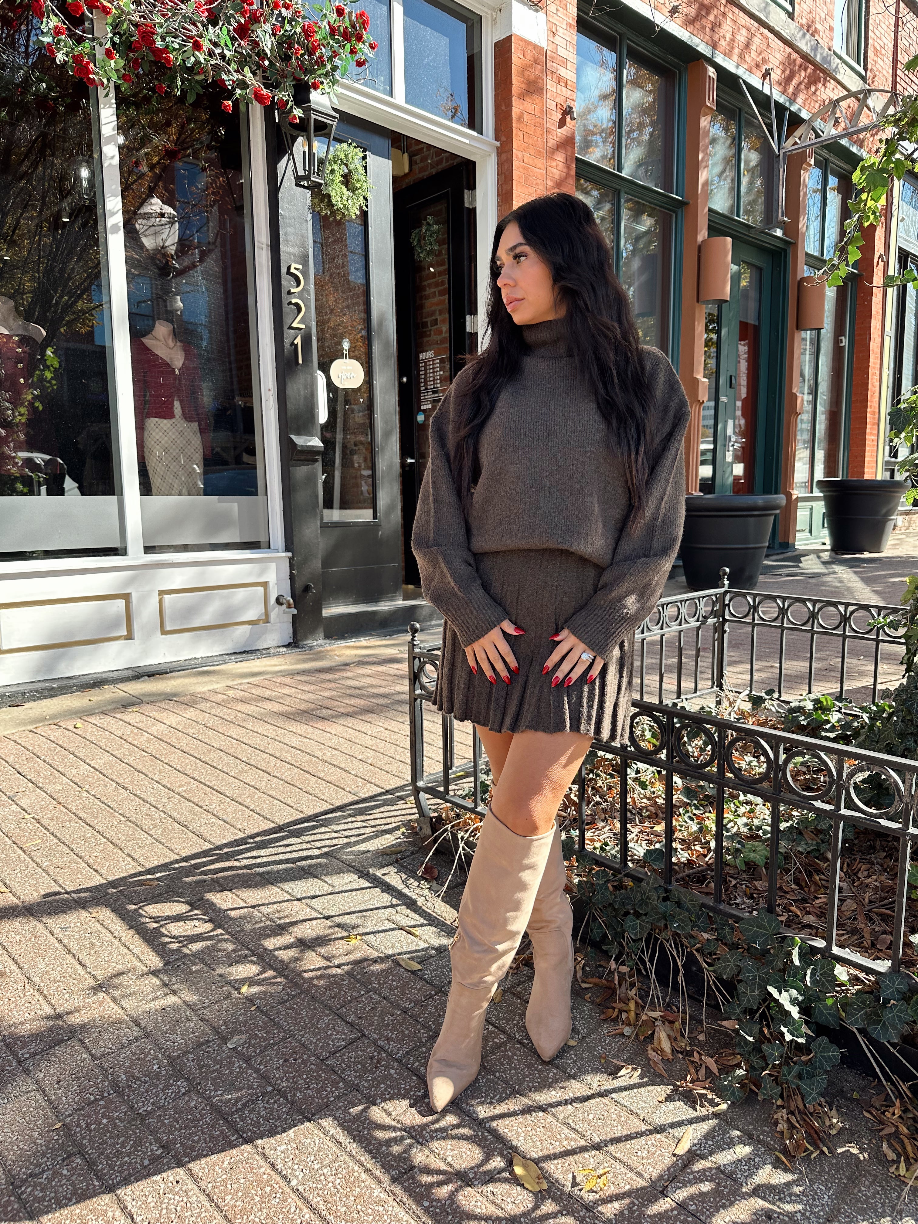 Woman wearing brown sweater two piece set with pleated mini skirt. 
