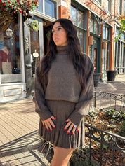 Woman wearing brown sweater two piece set with pleated mini skirt. 