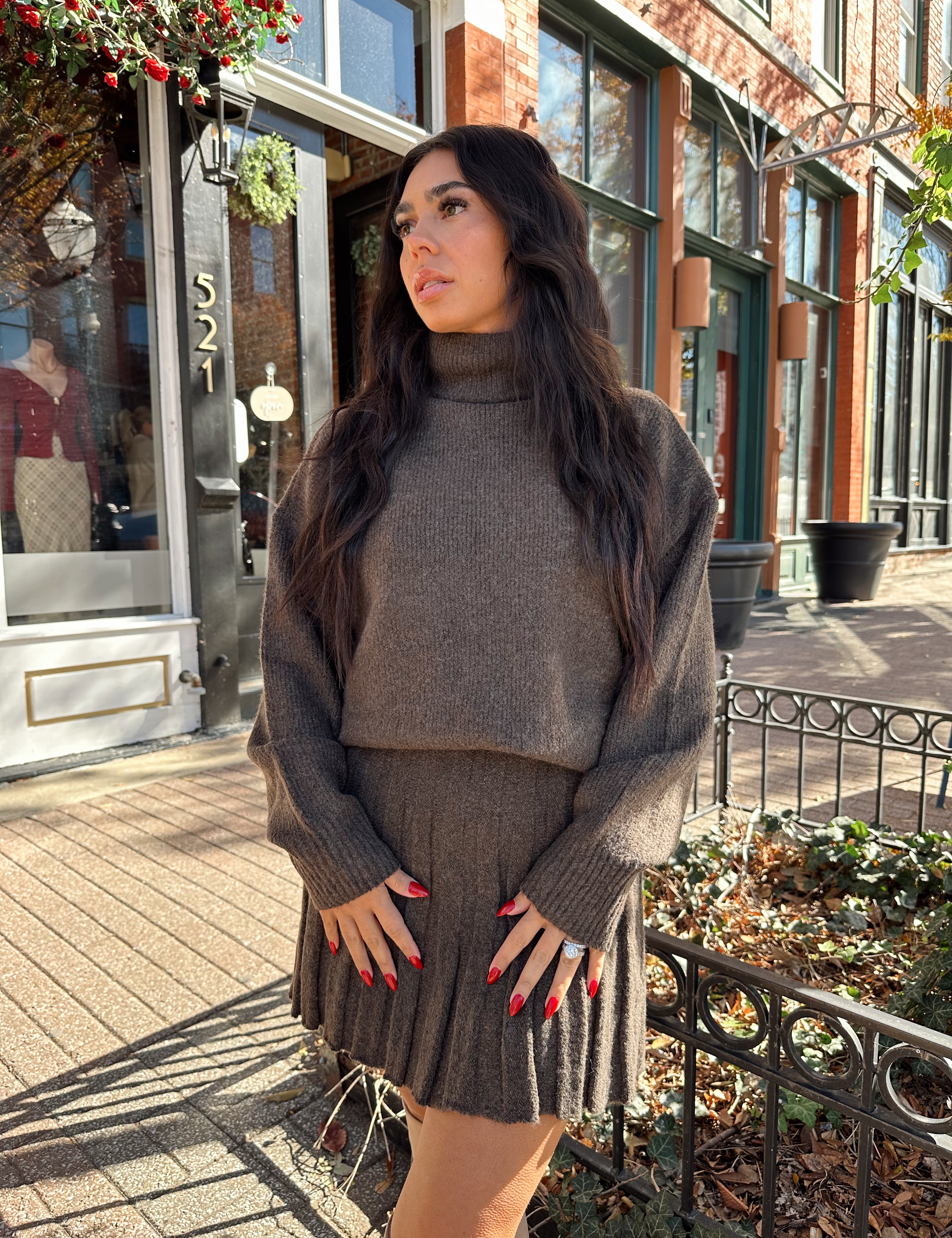 Woman wearing brown sweater two piece set with pleated mini skirt. 