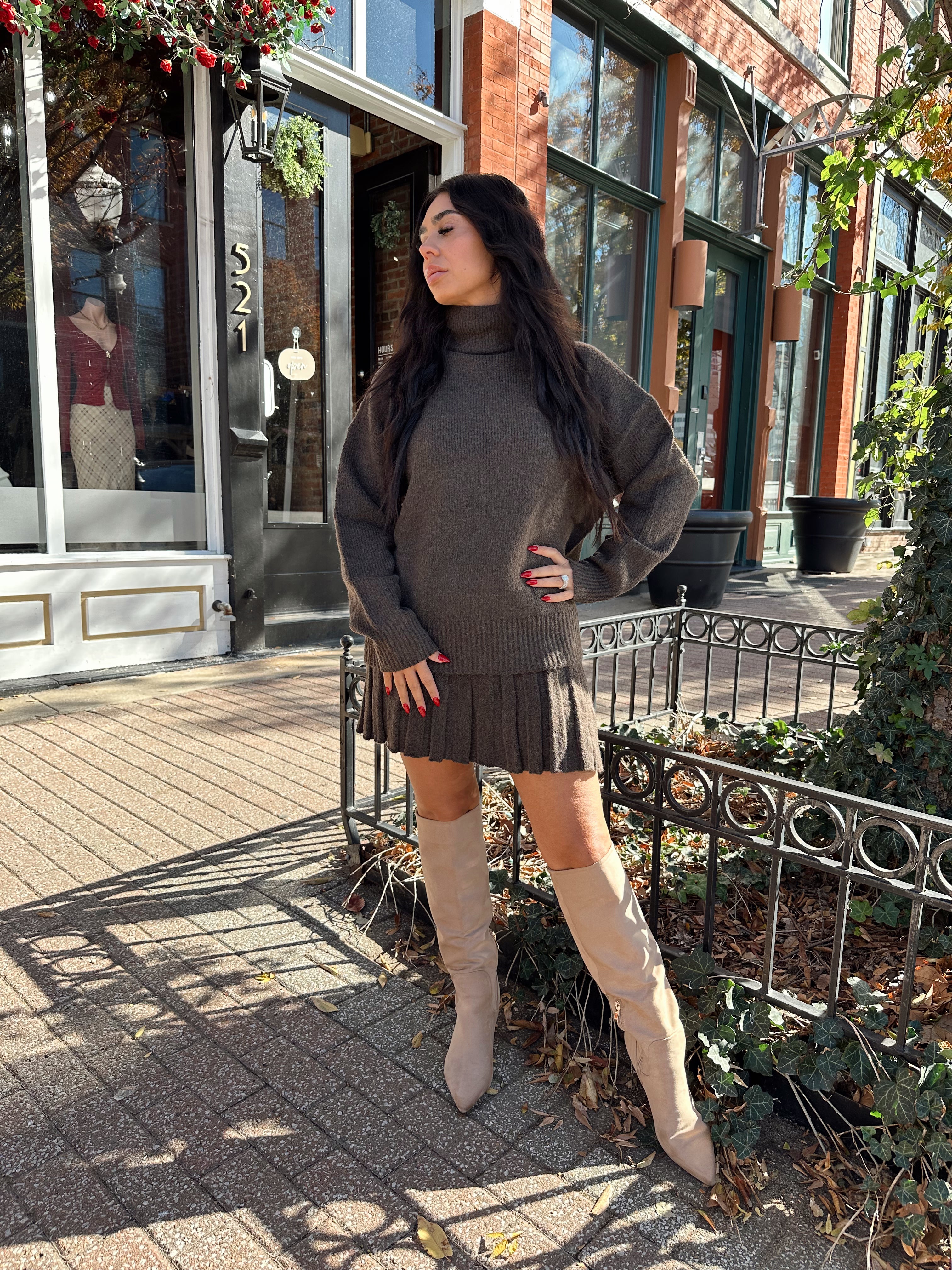 Woman wearing brown sweater two piece set with pleated mini skirt. 
