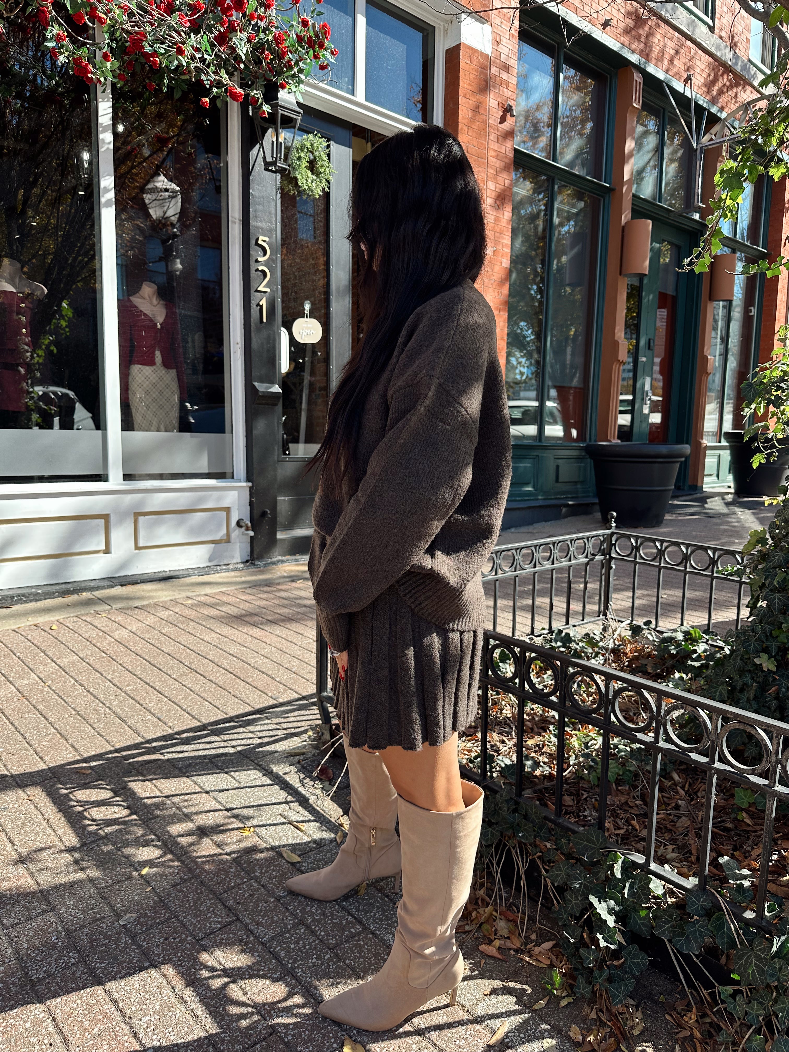Woman wearing brown sweater two piece set with pleated mini skirt. 