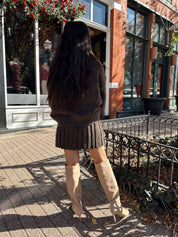 Woman wearing brown sweater two piece set with pleated mini skirt. 