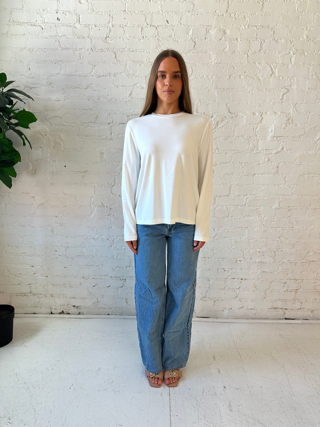 Woman wearing white long sleeve top with medium wash jeans.