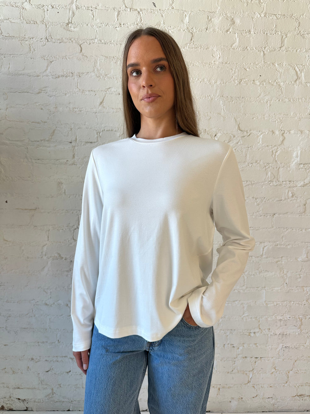 Woman wearing white long sleeve top with medium wash jeans.