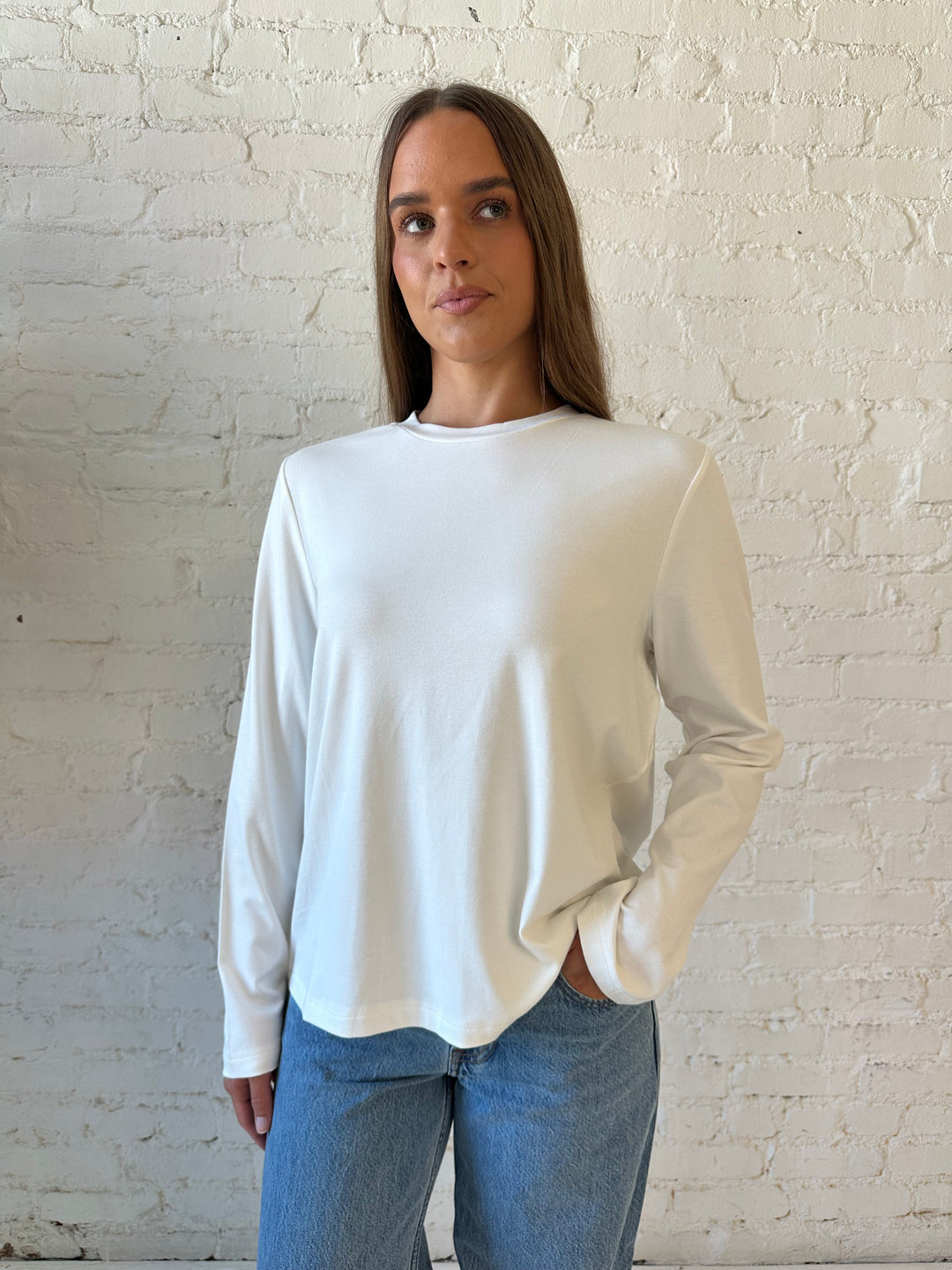 Woman wearing white long sleeve top with medium wash jeans.