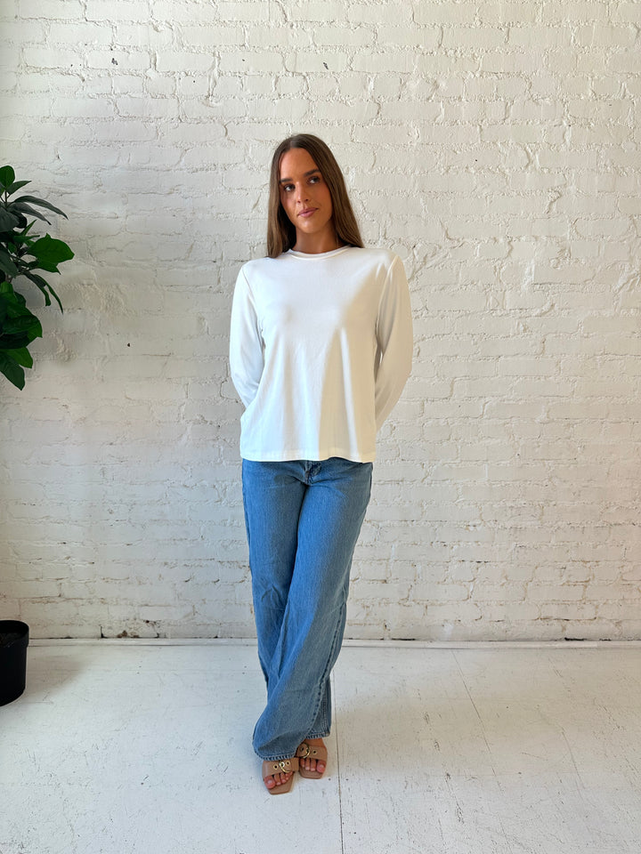 Woman wearing white long sleeve top with medium wash jeans.