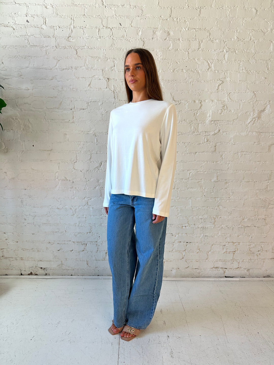 Woman wearing white long sleeve top with medium wash jeans.