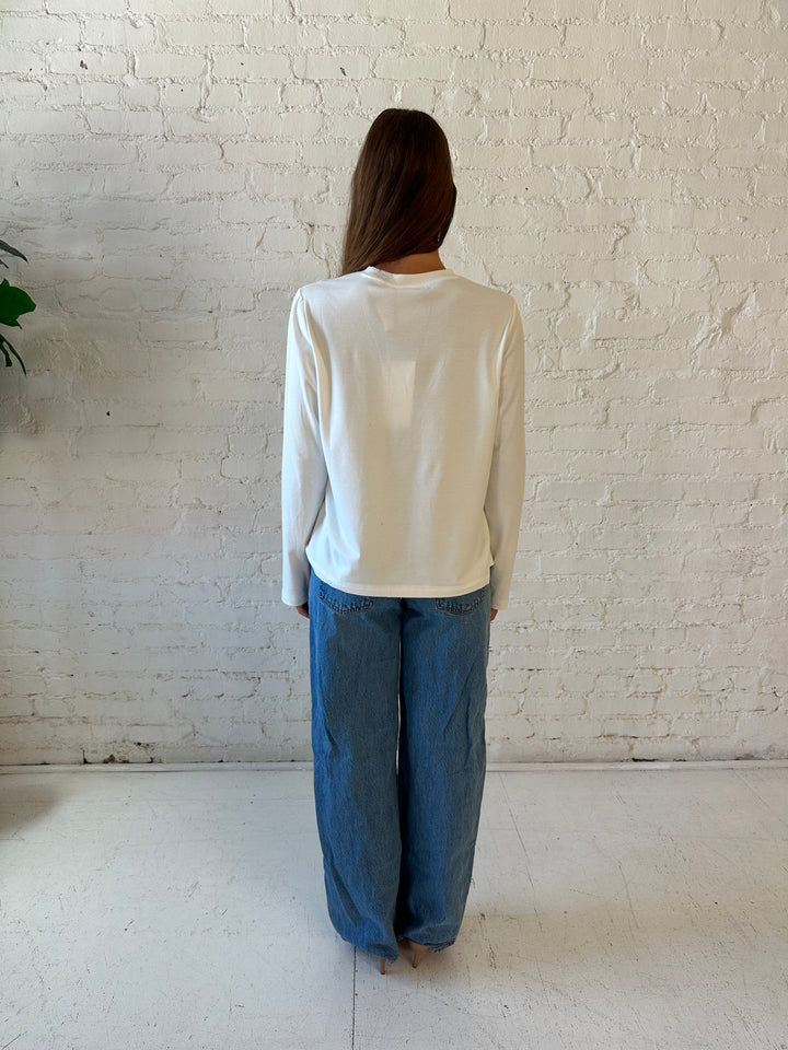 Woman wearing white long sleeve top with medium wash jeans.
