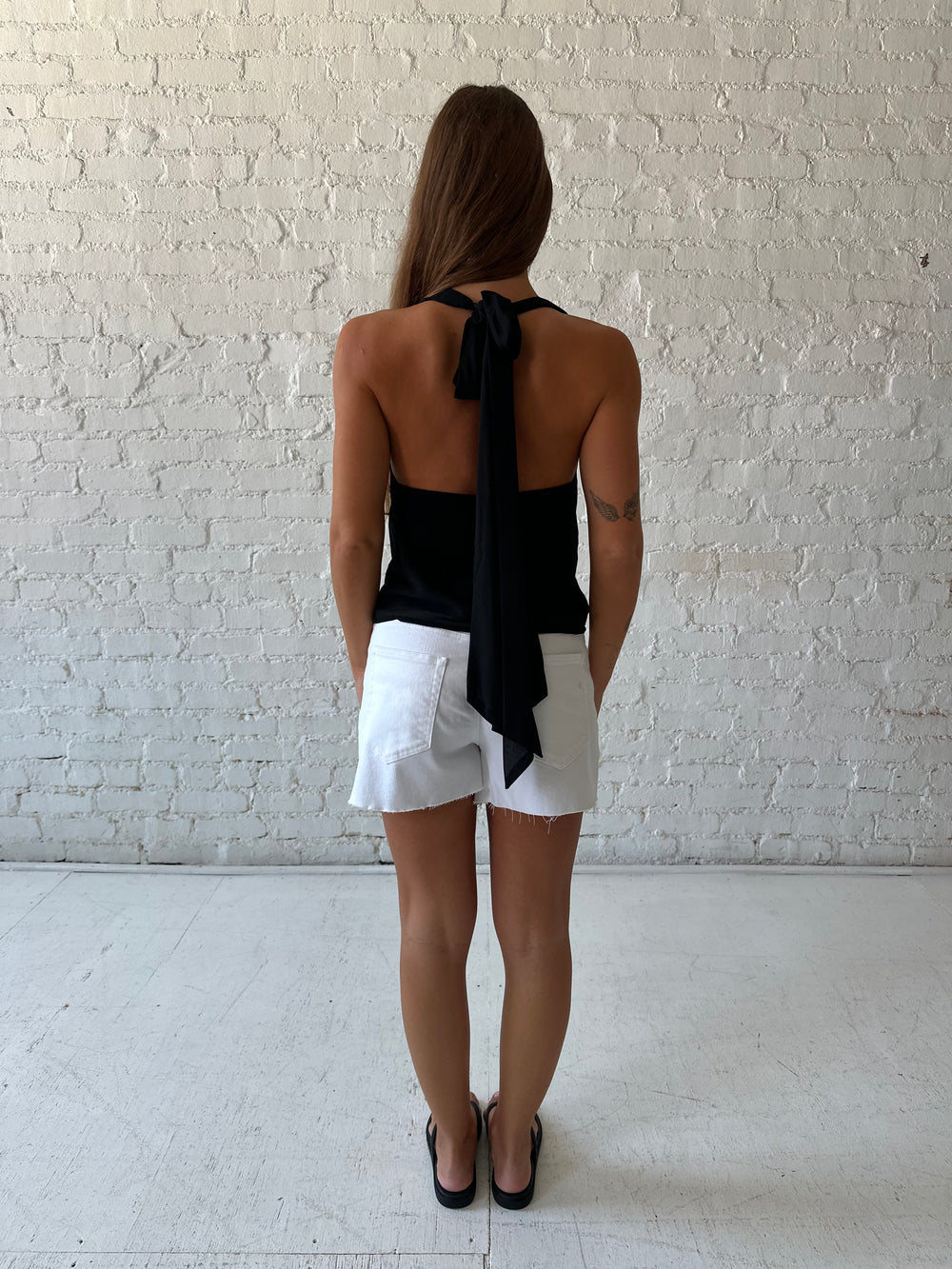 Woman wearing black halter cowl neck top with white denim shorts. 