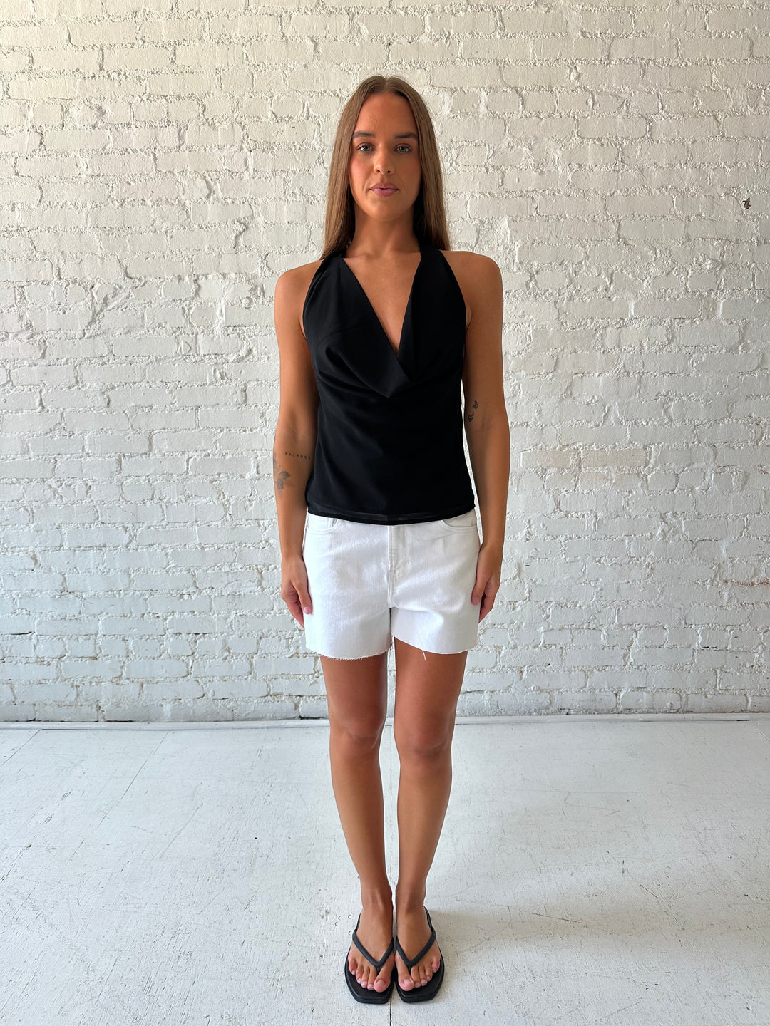 Woman wearing black halter cowl neck top with white denim shorts. 