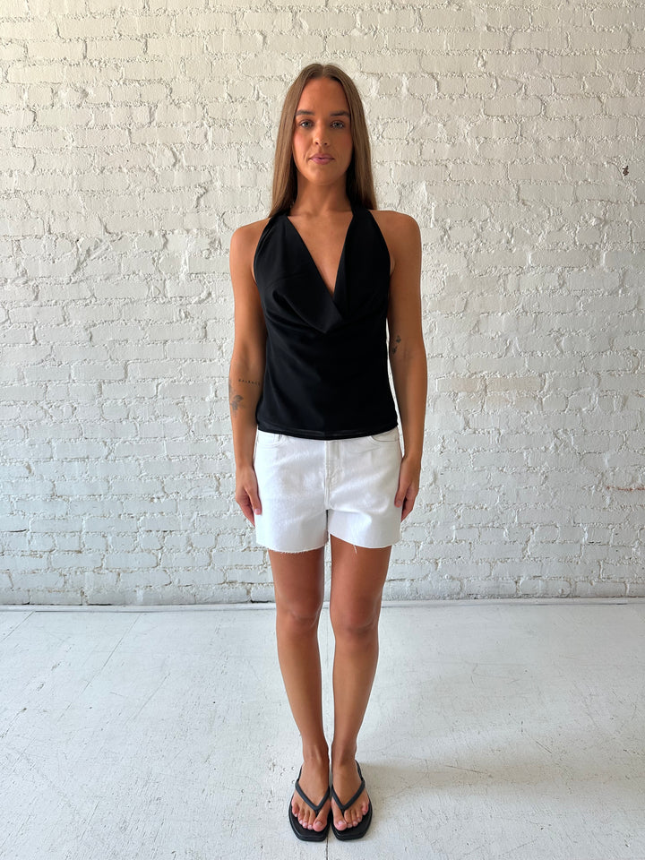 Woman wearing black halter cowl neck top with white denim shorts. 