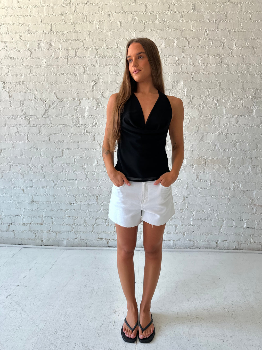 Woman wearing black halter cowl neck top with white denim shorts. 