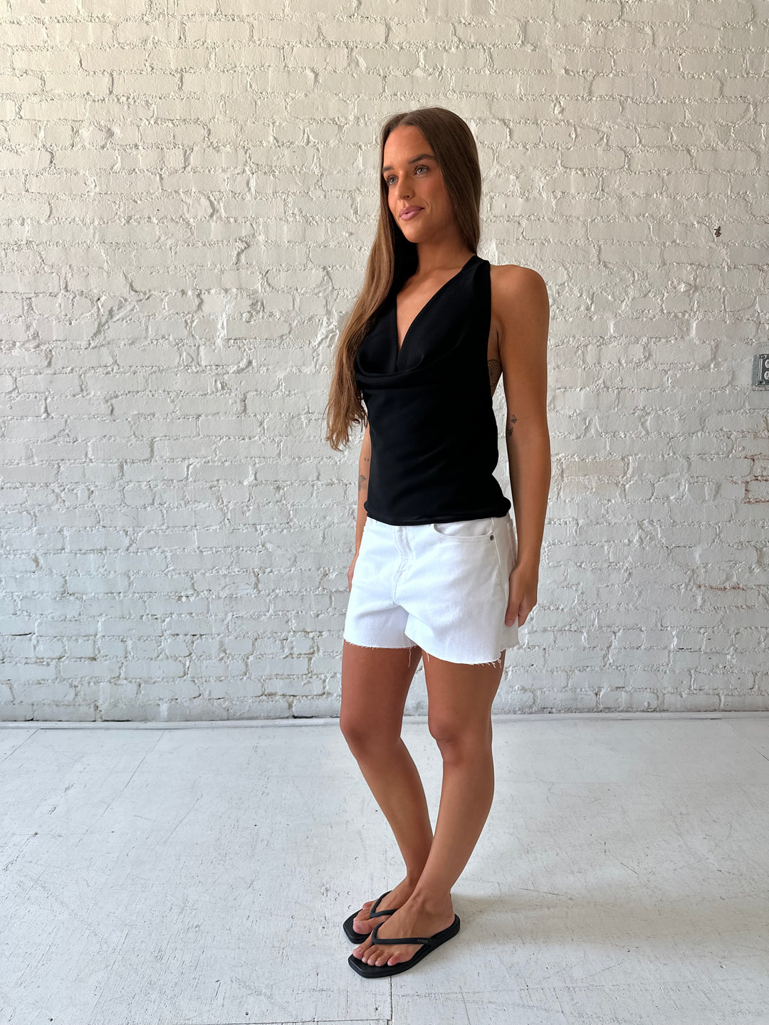 Woman wearing black halter cowl neck top with white denim shorts. 
