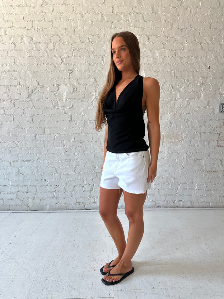 Woman wearing black halter cowl neck top with white denim shorts. 
