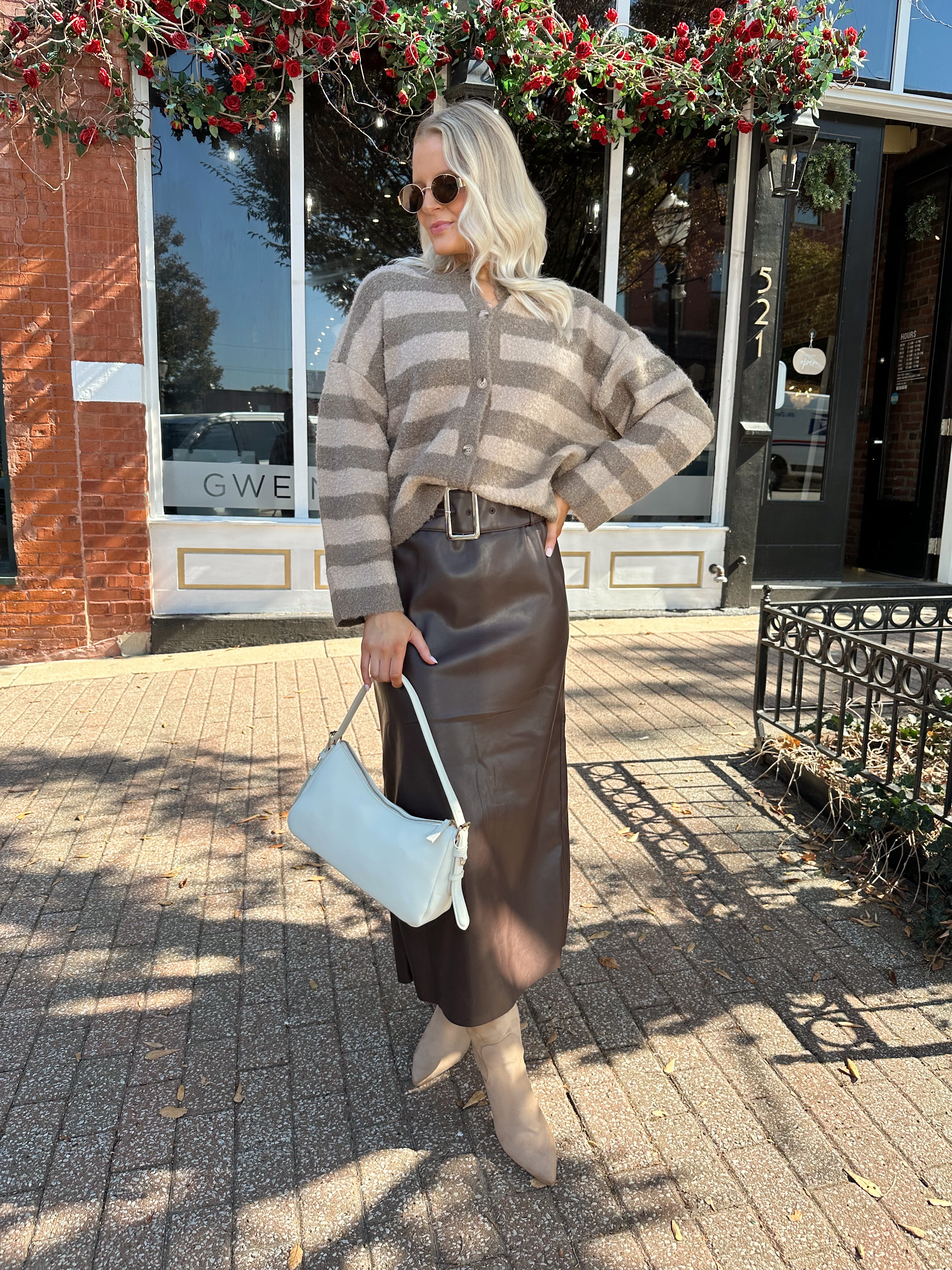 Woman wearing brown striped cardigan and dark brown leather skirt. 