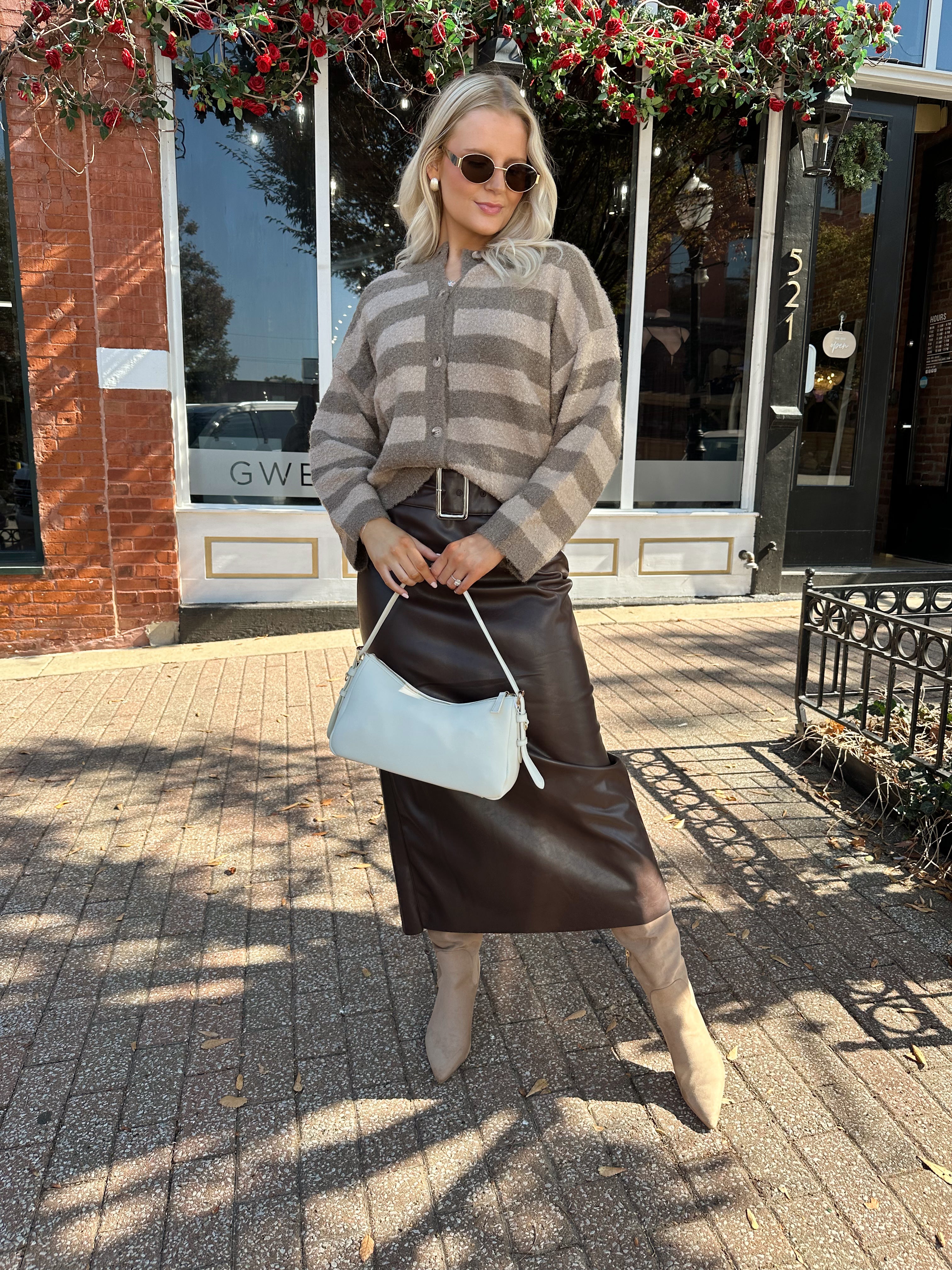 Woman wearing brown striped cardigan and dark brown leather skirt. 