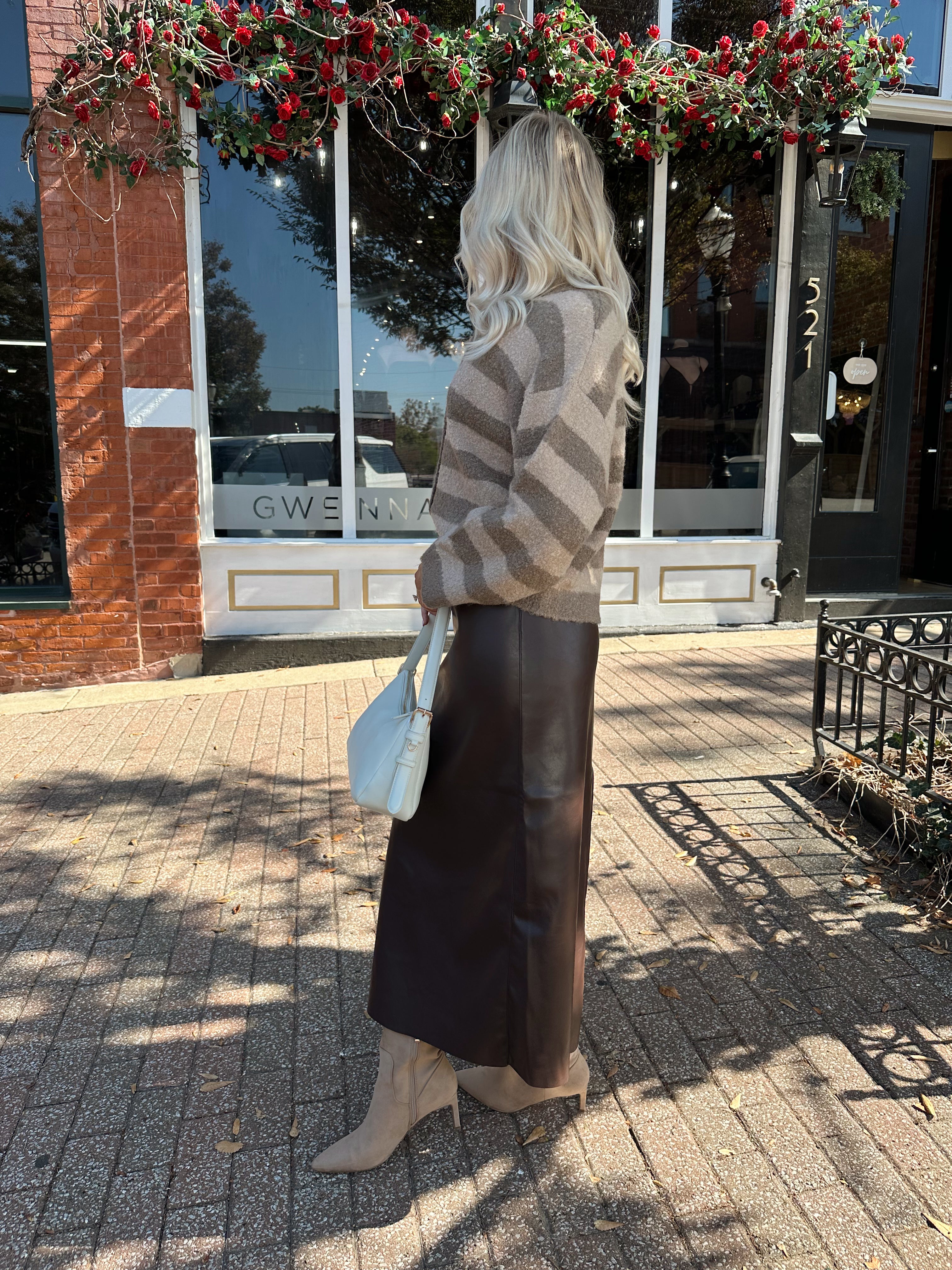 Woman wearing brown striped cardigan and dark brown leather skirt. 