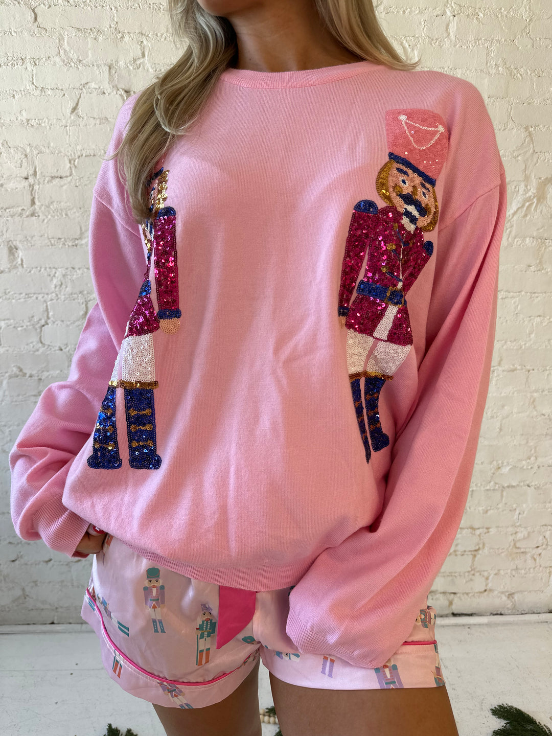 Woman wearing blush pink knit crewneck sweater with oversized sequin nutcrackers.
