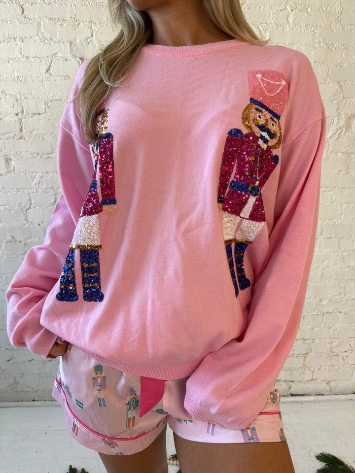 Woman wearing blush pink knit crewneck sweater with oversized sequin nutcrackers.