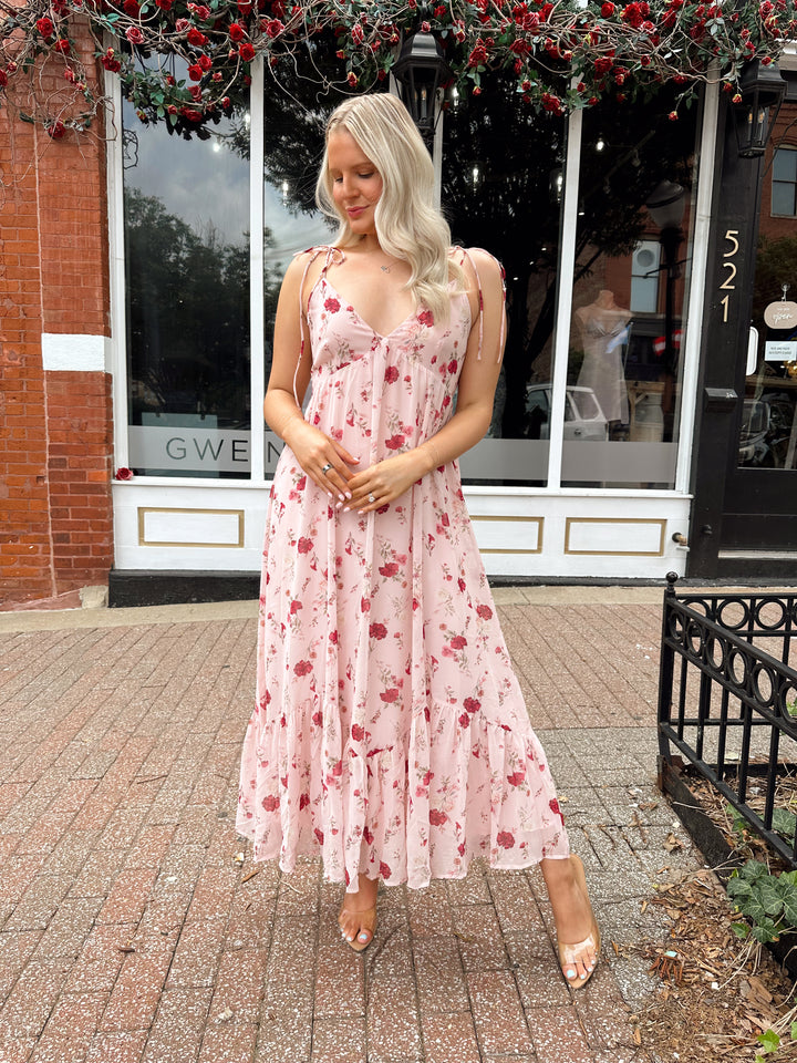 Woman wearing light pink maxi dress with floral pattern all over. 