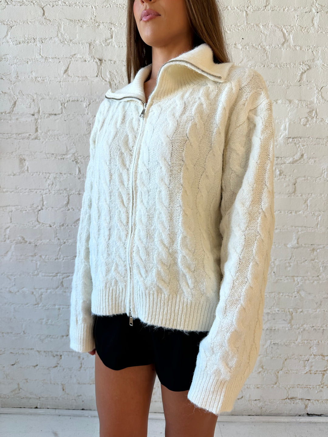 Woman wearing cream fuzzy cable knit zip up jacket with black leather shorts. 