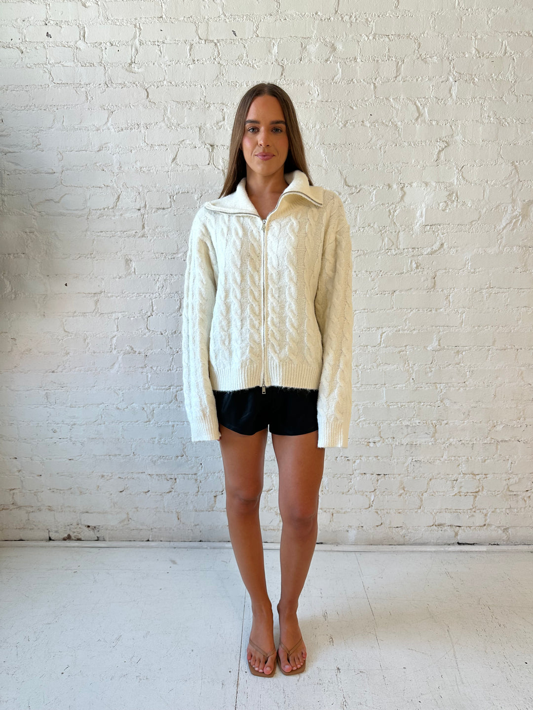 Woman wearing cream fuzzy cable knit zip up jacket with black leather shorts. 