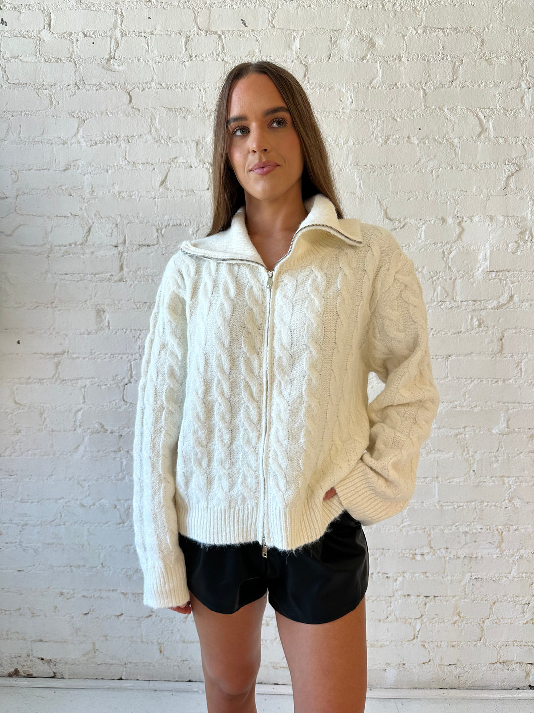 Woman wearing cream fuzzy cable knit zip up jacket with black leather shorts. 