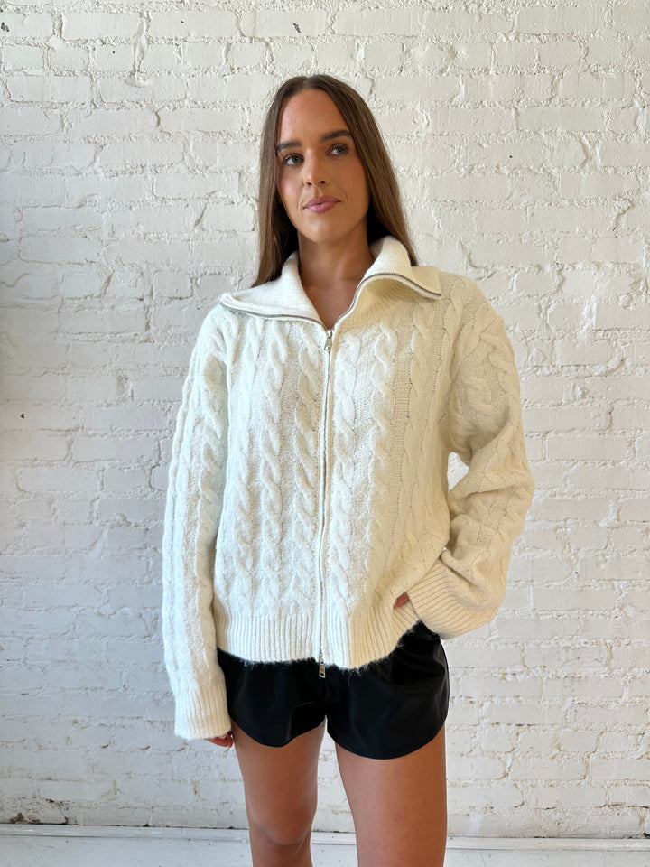 Woman wearing cream fuzzy cable knit zip up jacket with black leather shorts. 