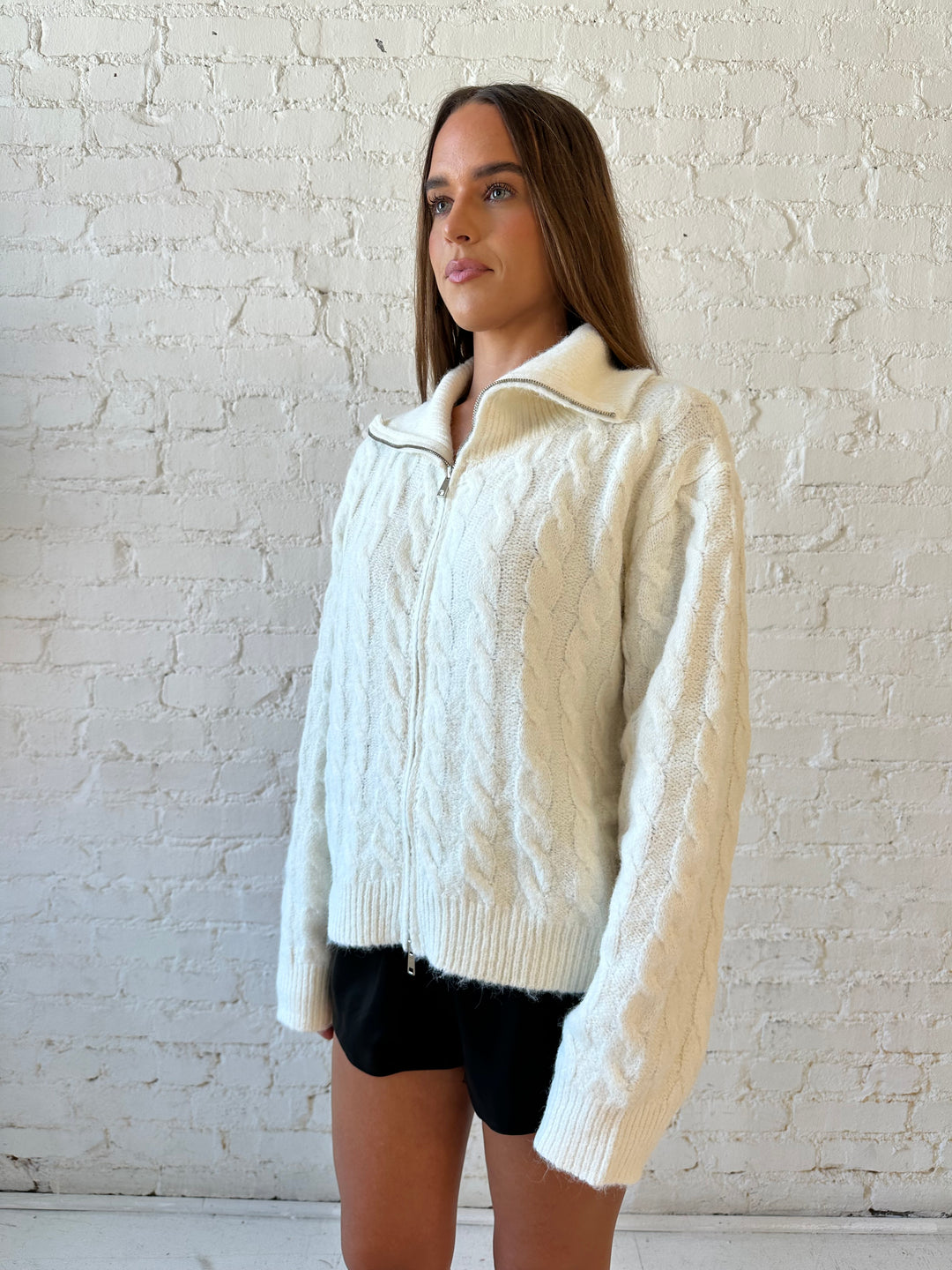 Woman wearing cream fuzzy cable knit zip up jacket with black leather shorts. 
