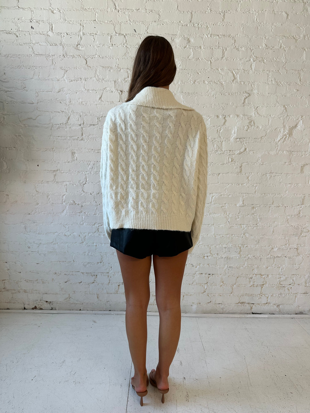 Woman wearing cream fuzzy cable knit zip up jacket with black leather shorts. 