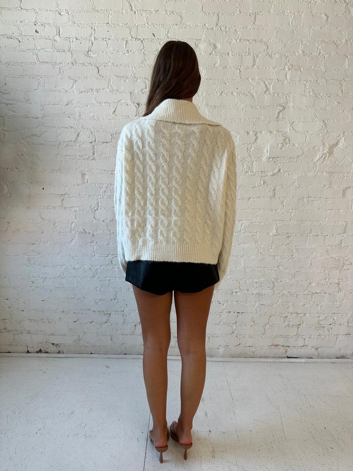 Woman wearing cream fuzzy cable knit zip up jacket with black leather shorts. 