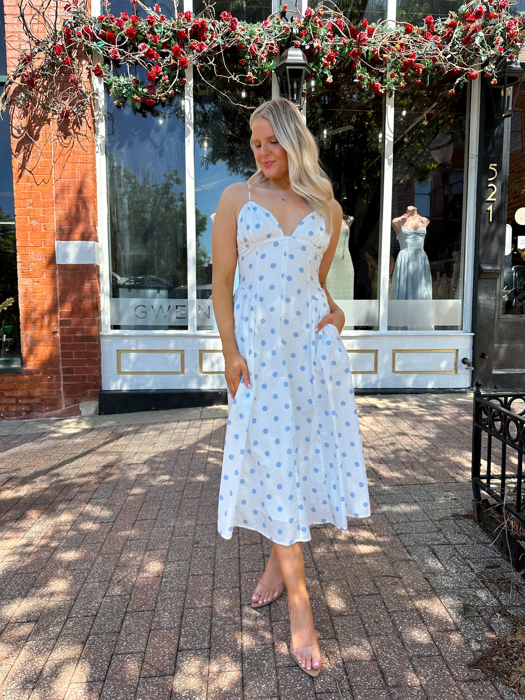 Woman wearing white midi dress with light blue polka dots and adjustable spaghetti straps.