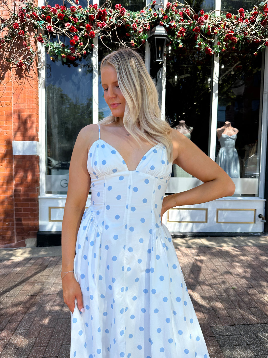 Woman wearing white midi dress with light blue polka dots and adjustable spaghetti straps.