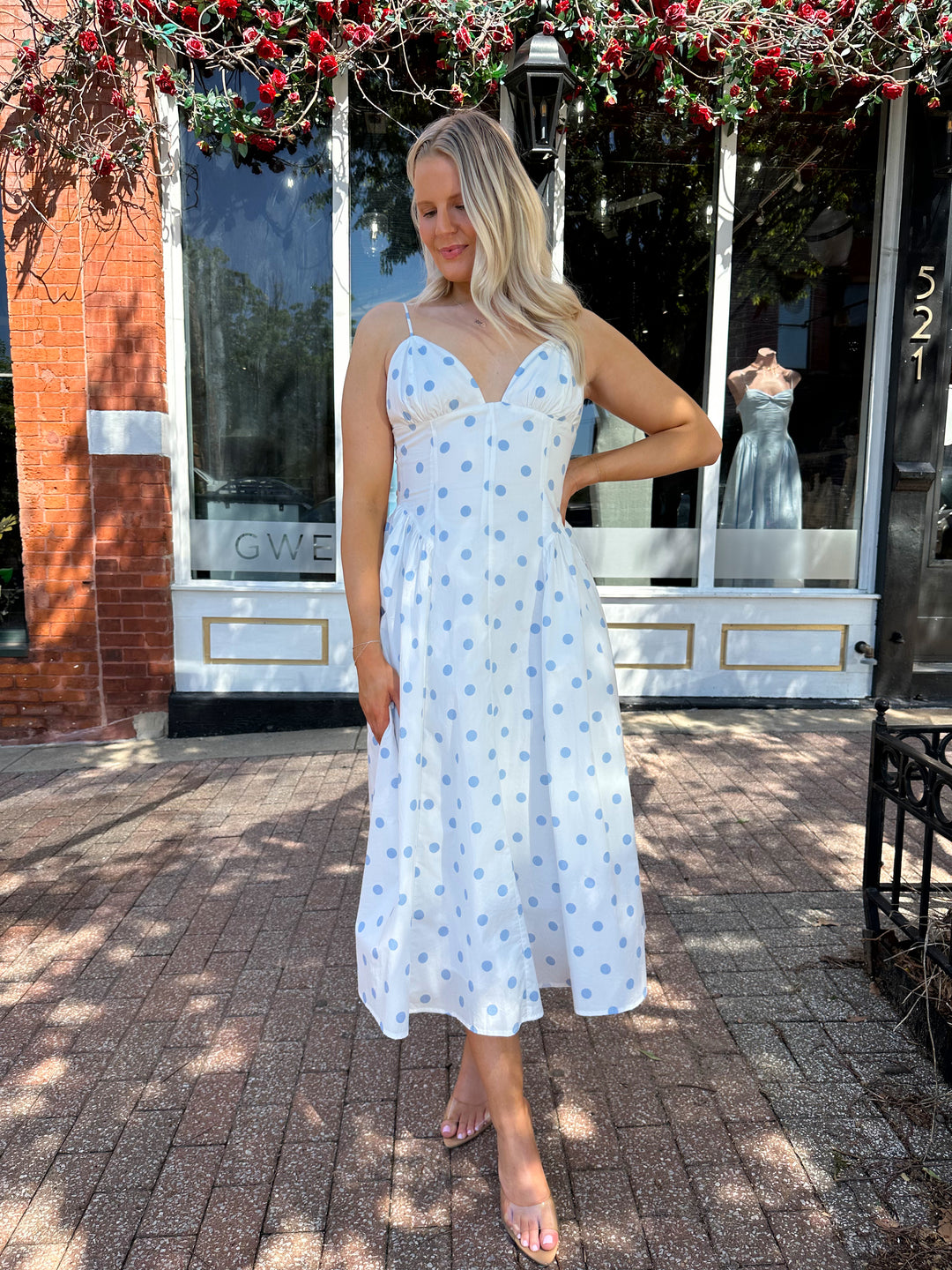 Woman wearing white midi dress with light blue polka dots and adjustable spaghetti straps.