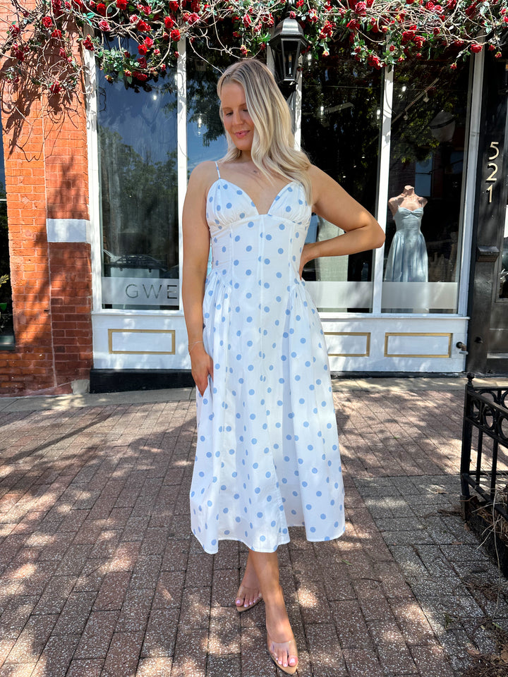 Woman wearing white midi dress with light blue polka dots and adjustable spaghetti straps.