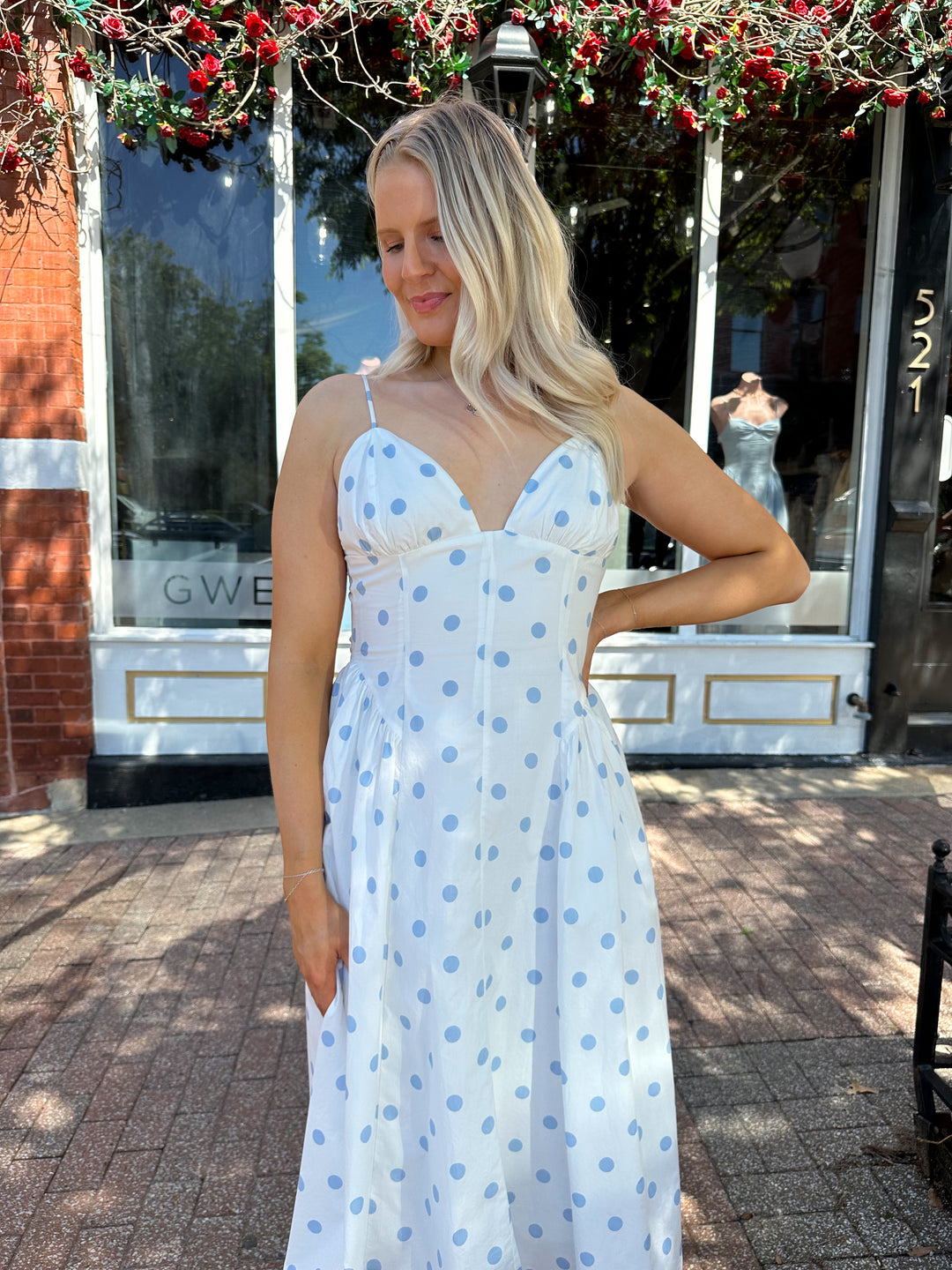 Woman wearing white midi dress with light blue polka dots and adjustable spaghetti straps.