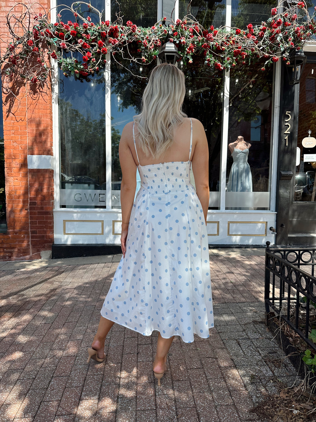 Woman wearing white midi dress with light blue polka dots and adjustable spaghetti straps.