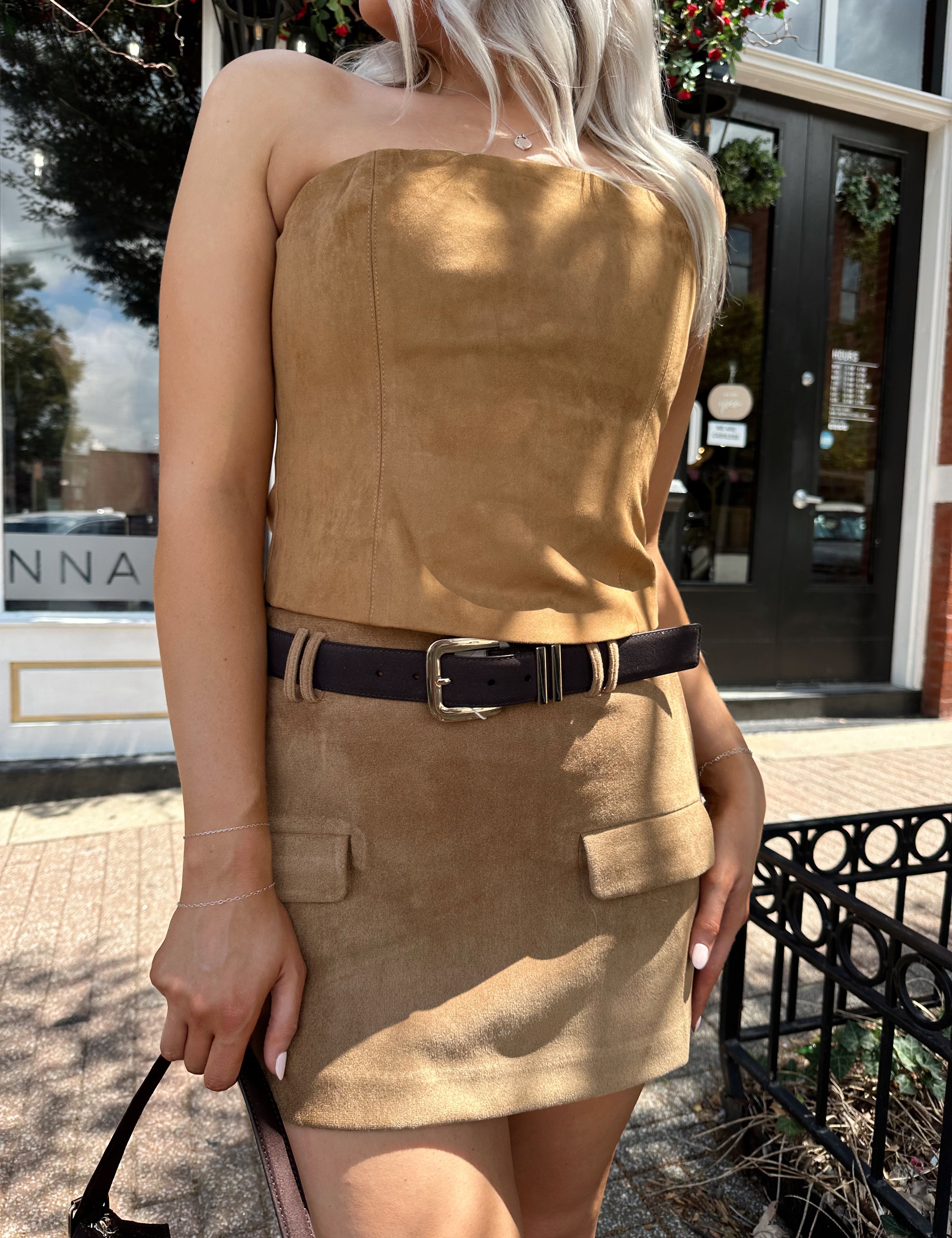 Woman wearing tan suede mini skirt with faux pockets and a brown suede belt.