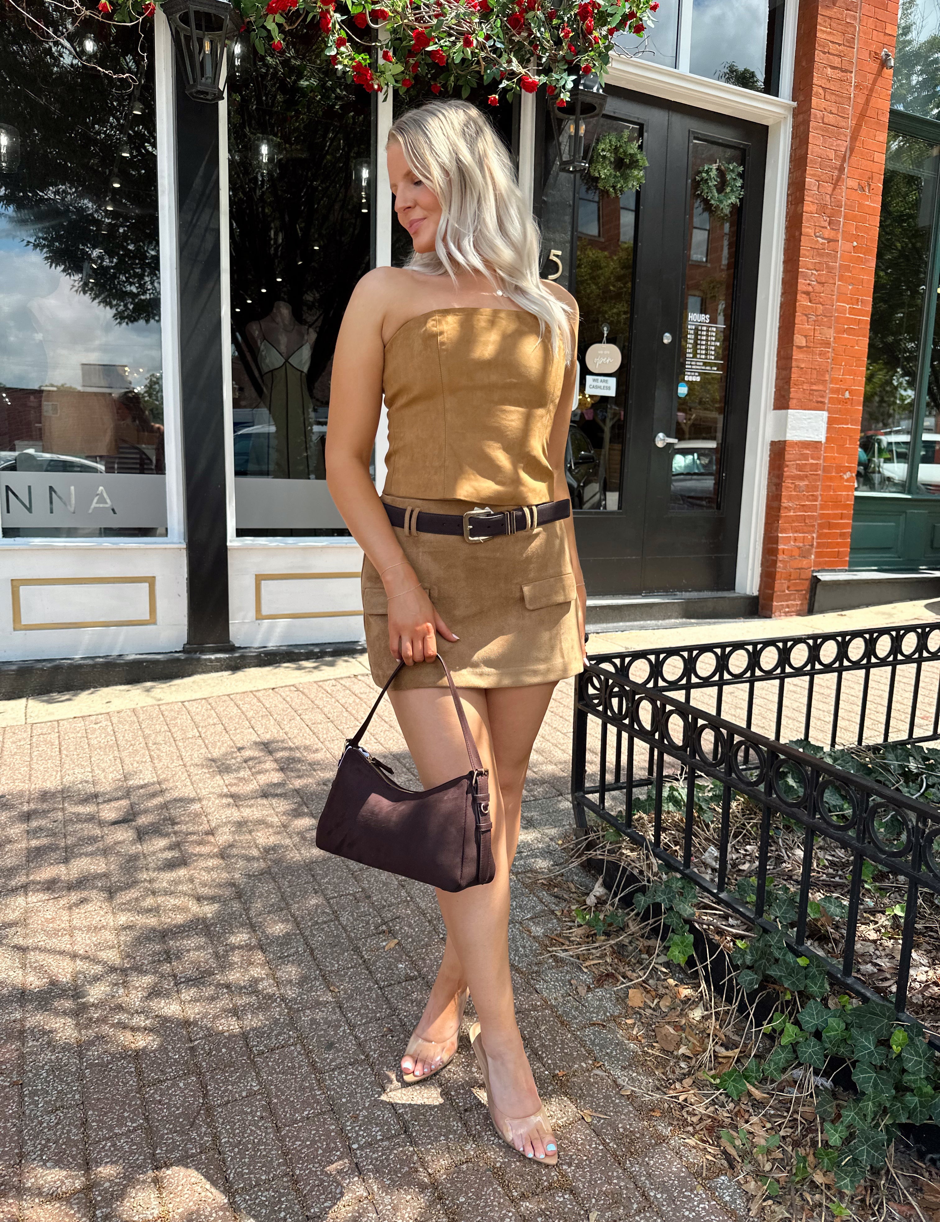 Woman wearing tan suede mini skirt with faux pockets and a brown suede belt.