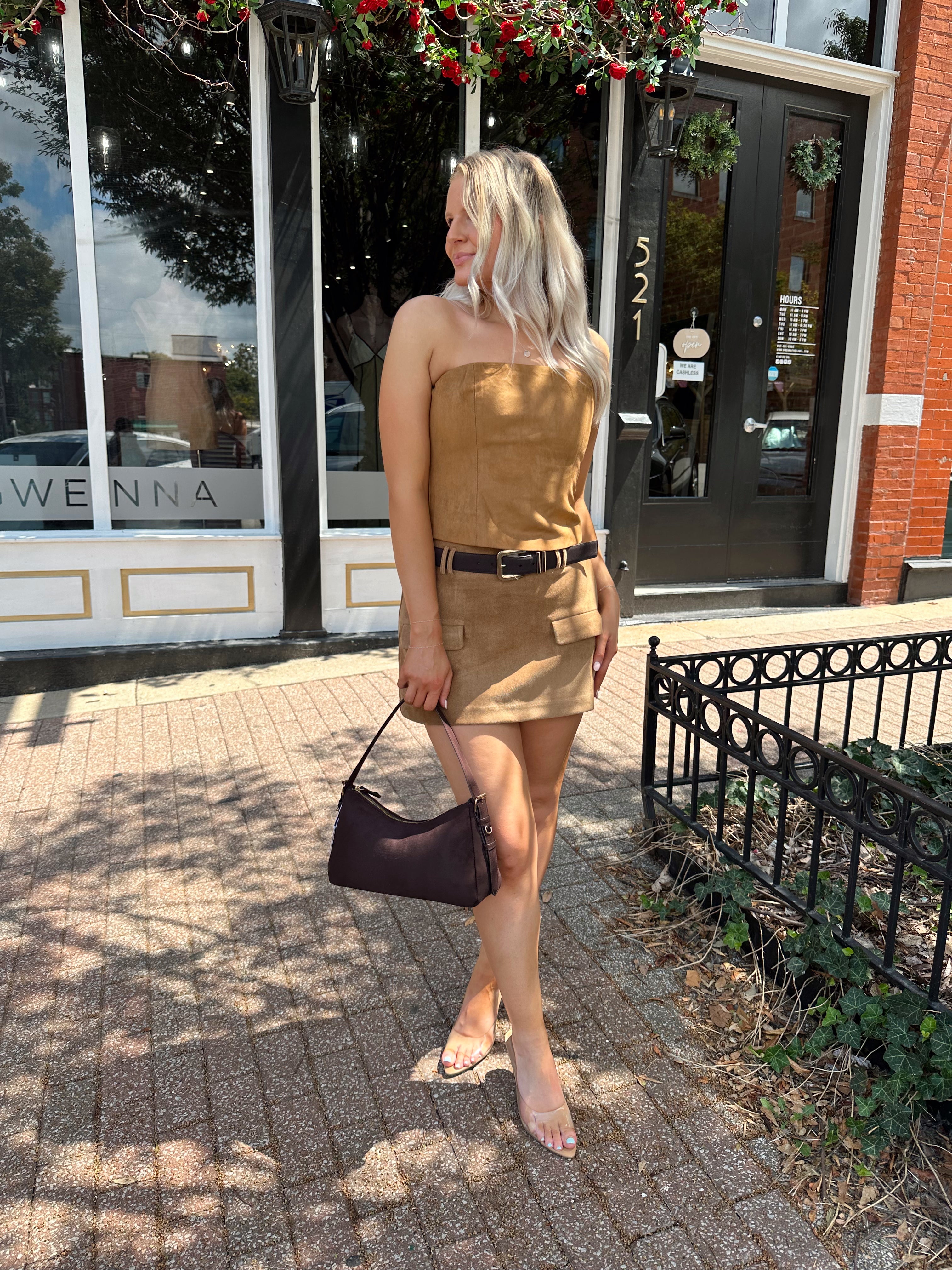 Woman wearing tan suede mini skirt with faux pockets and a brown suede belt.