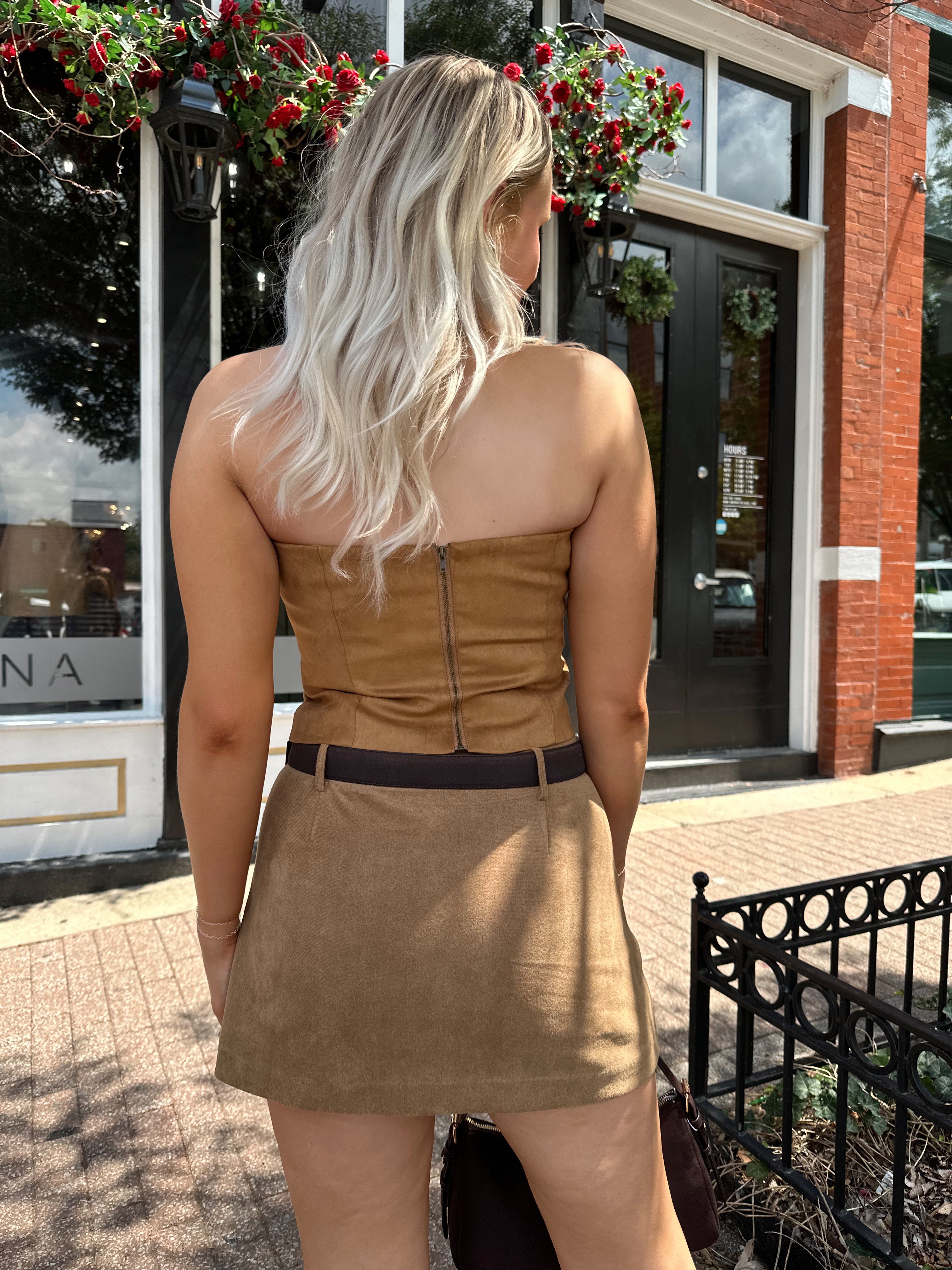 Woman wearing tan suede mini skirt with faux pockets and a brown suede belt.