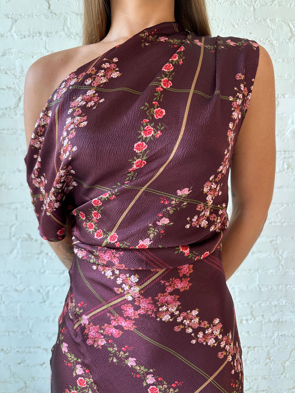 Woman wearing burgundy floral satin maxi dress with asymmetrical neckline, and flutter hem.