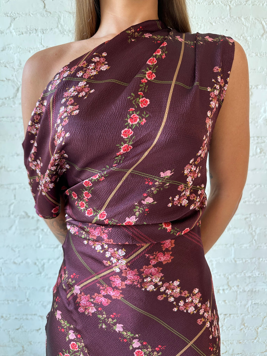 Woman wearing burgundy floral satin maxi dress with asymmetrical neckline, and flutter hem.