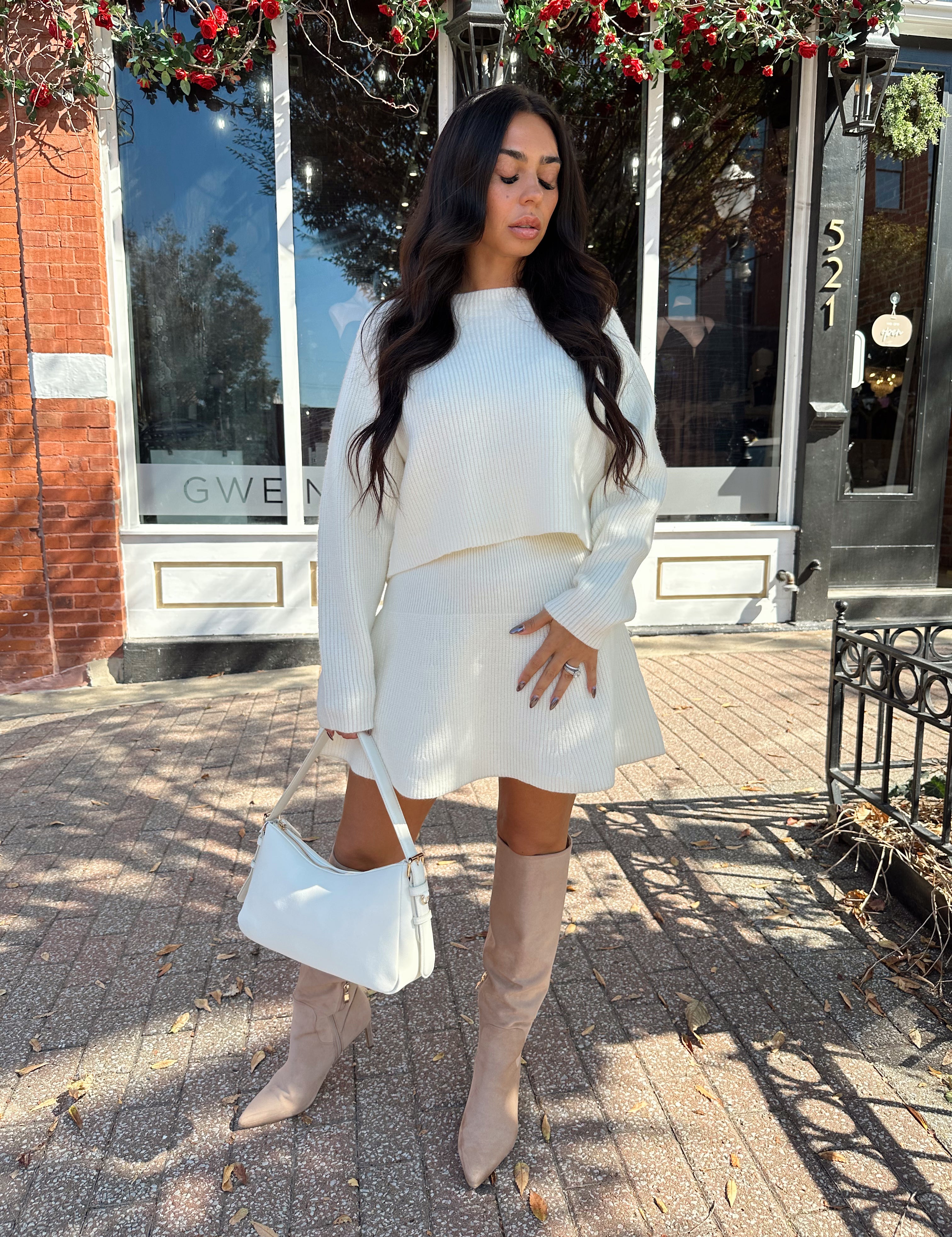 Woman wearing cream sweater two piece set with long sleeve top and mini skirt. 