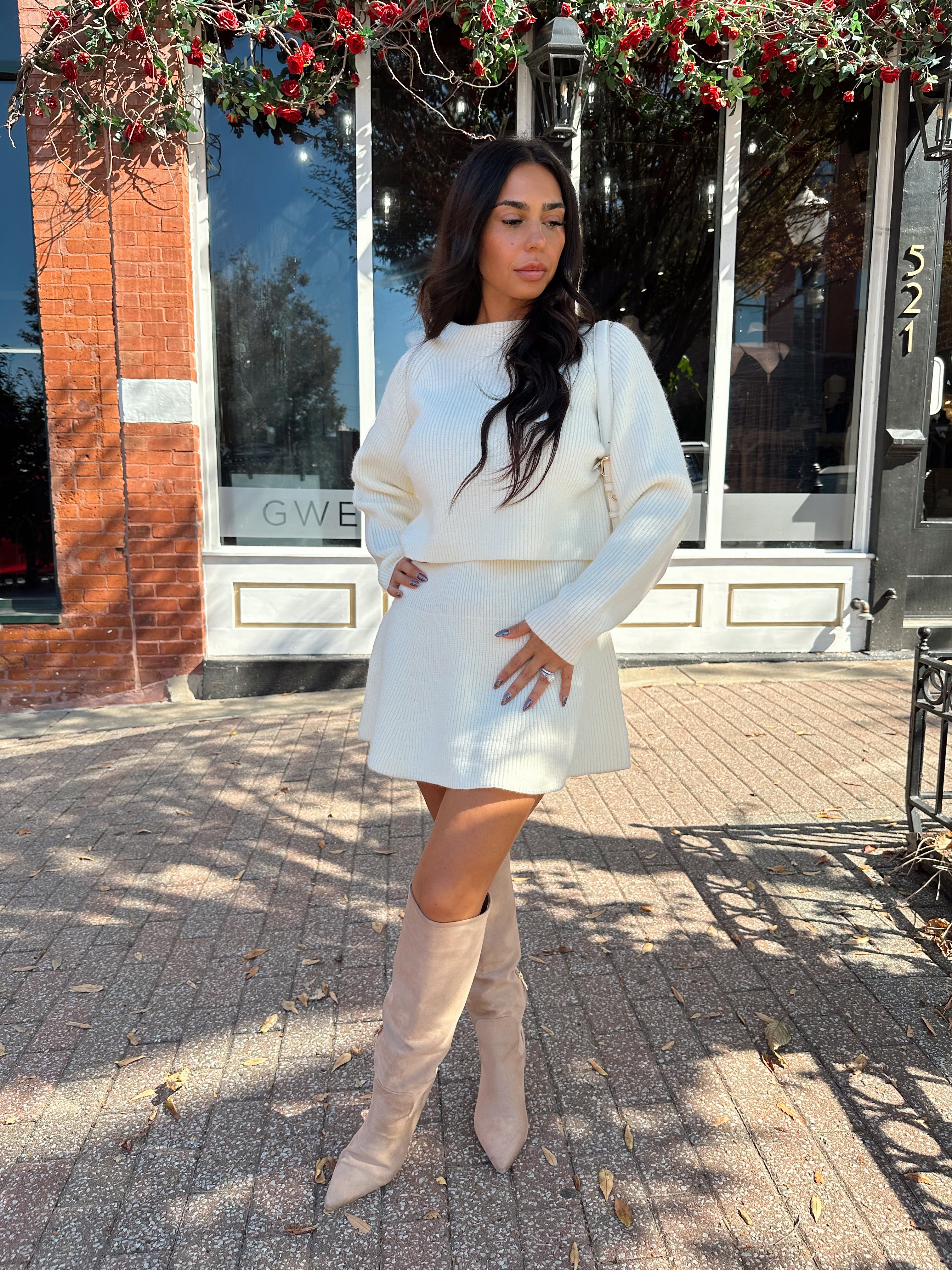 Woman wearing cream sweater two piece set with long sleeve top and mini skirt. 
