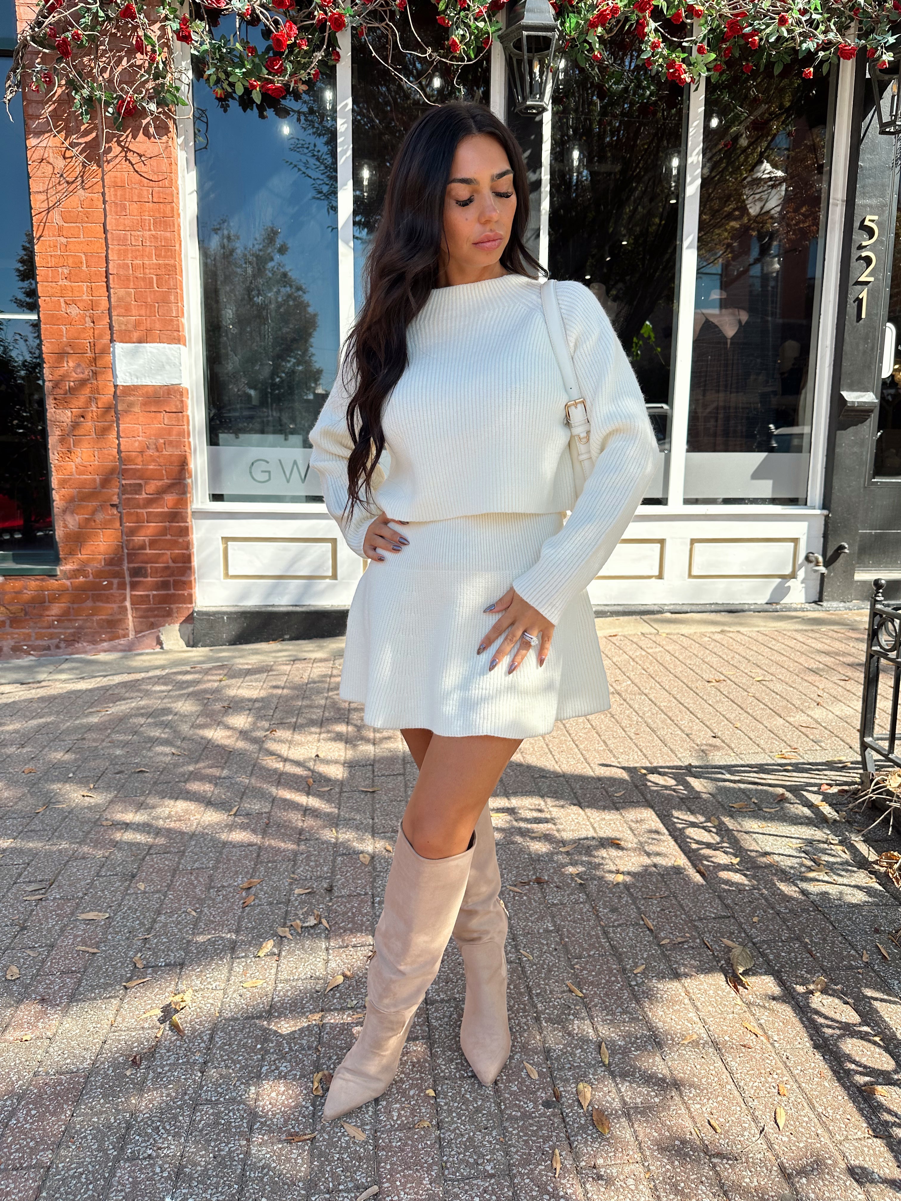 Woman wearing cream sweater two piece set with long sleeve top and mini skirt. 