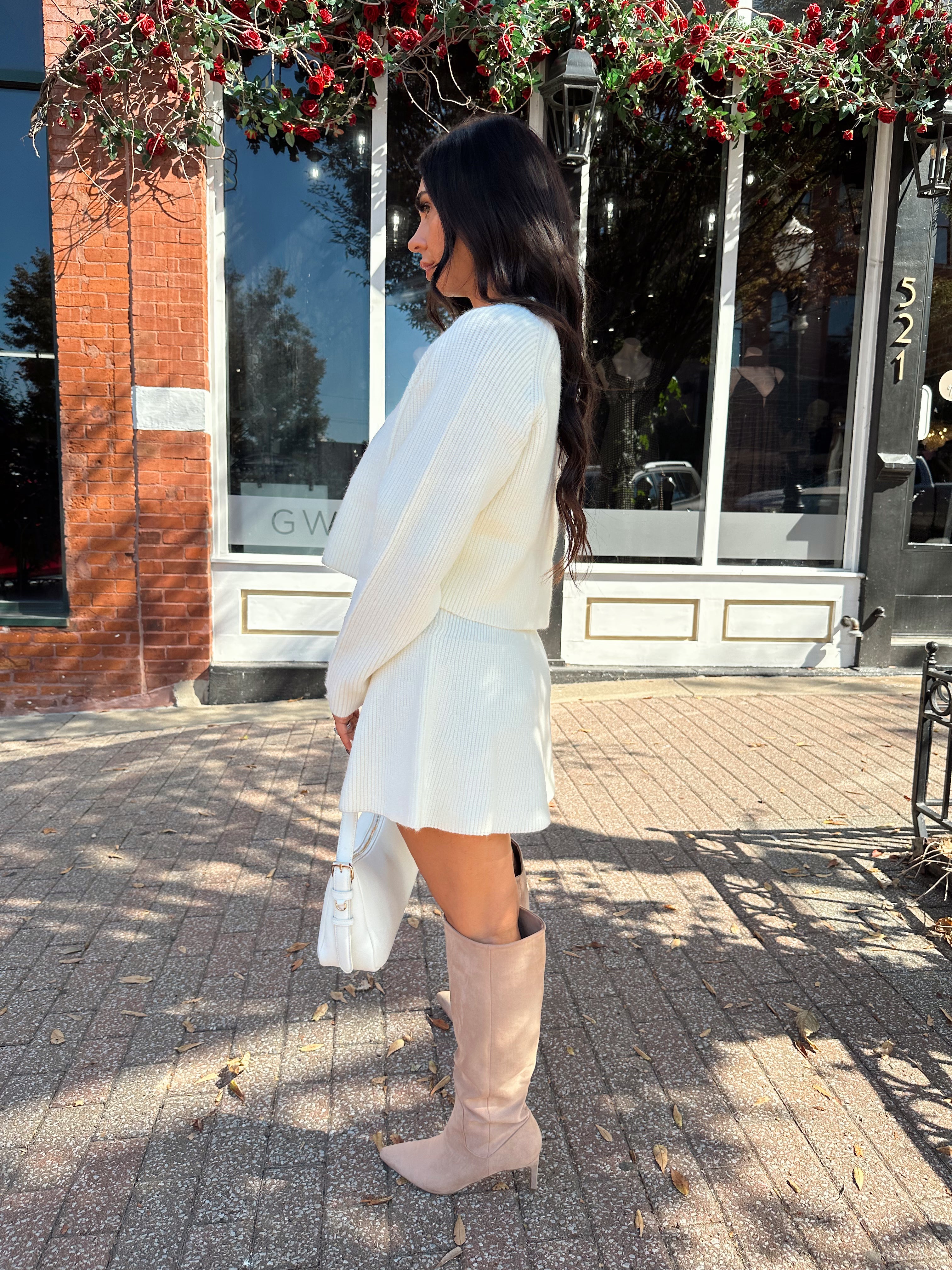 Woman wearing cream sweater two piece set with long sleeve top and mini skirt. 