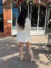 Woman wearing cream sweater two piece set with long sleeve top and mini skirt. 