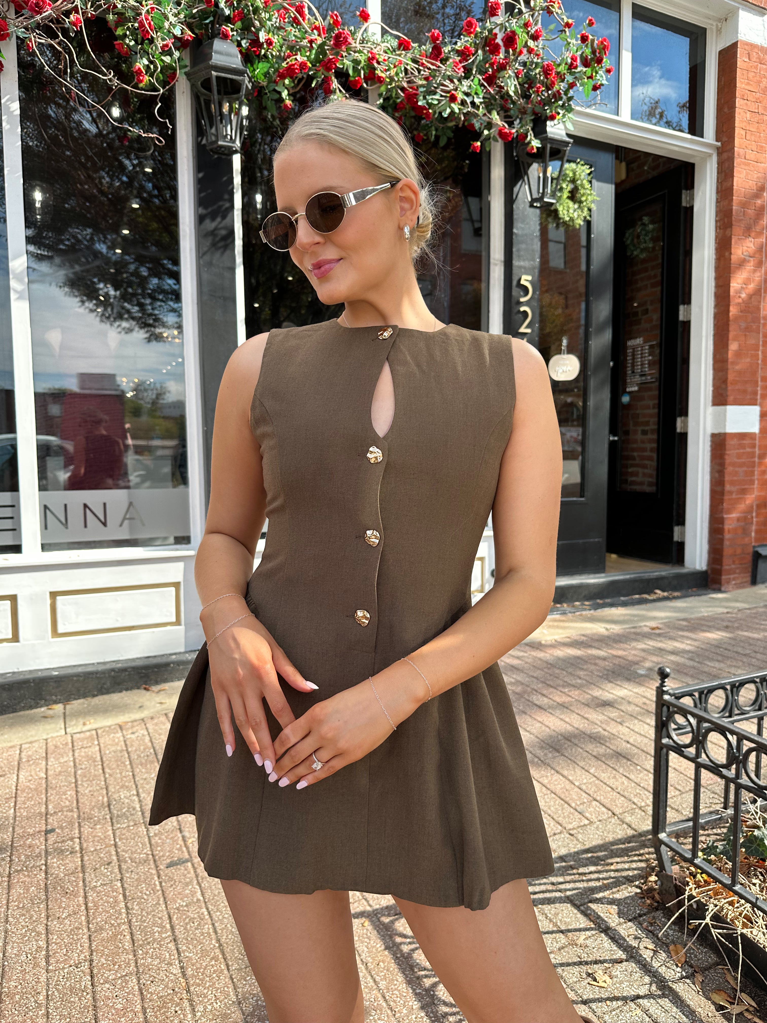 Woman wearing brown fit to flare mini dress with keyhole cutout and gold buttons.
